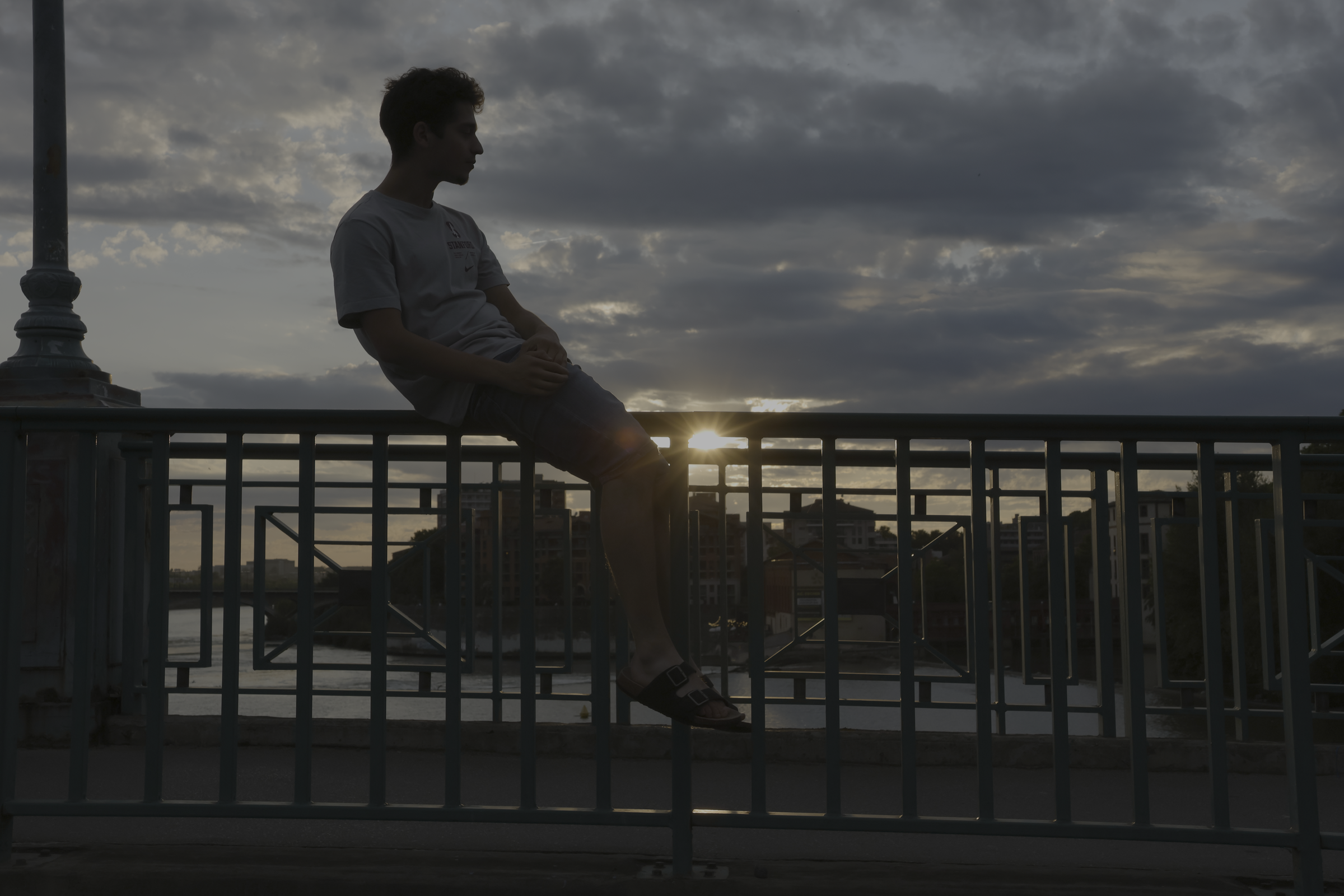 Silhouette assise sur une rambarde au bord de l’eau dans la lumière du soir